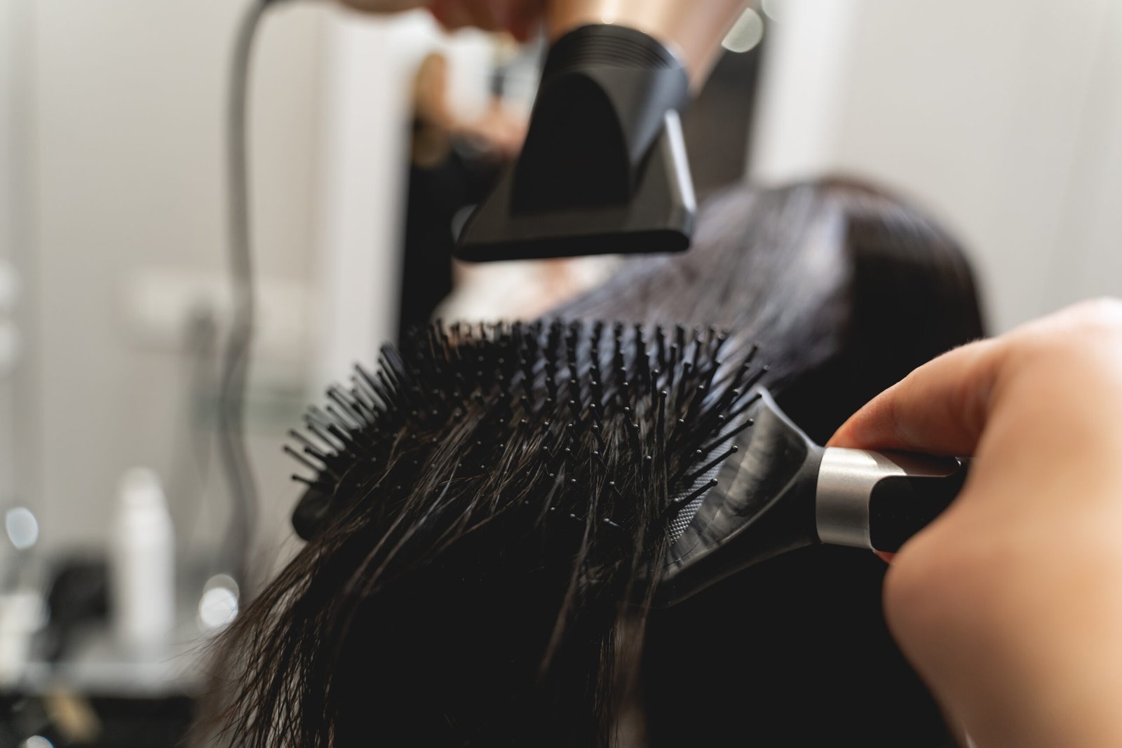 Individual at a salon blow drying their client's hair, skilfully using a hair dryer and comb for a stylish finish.