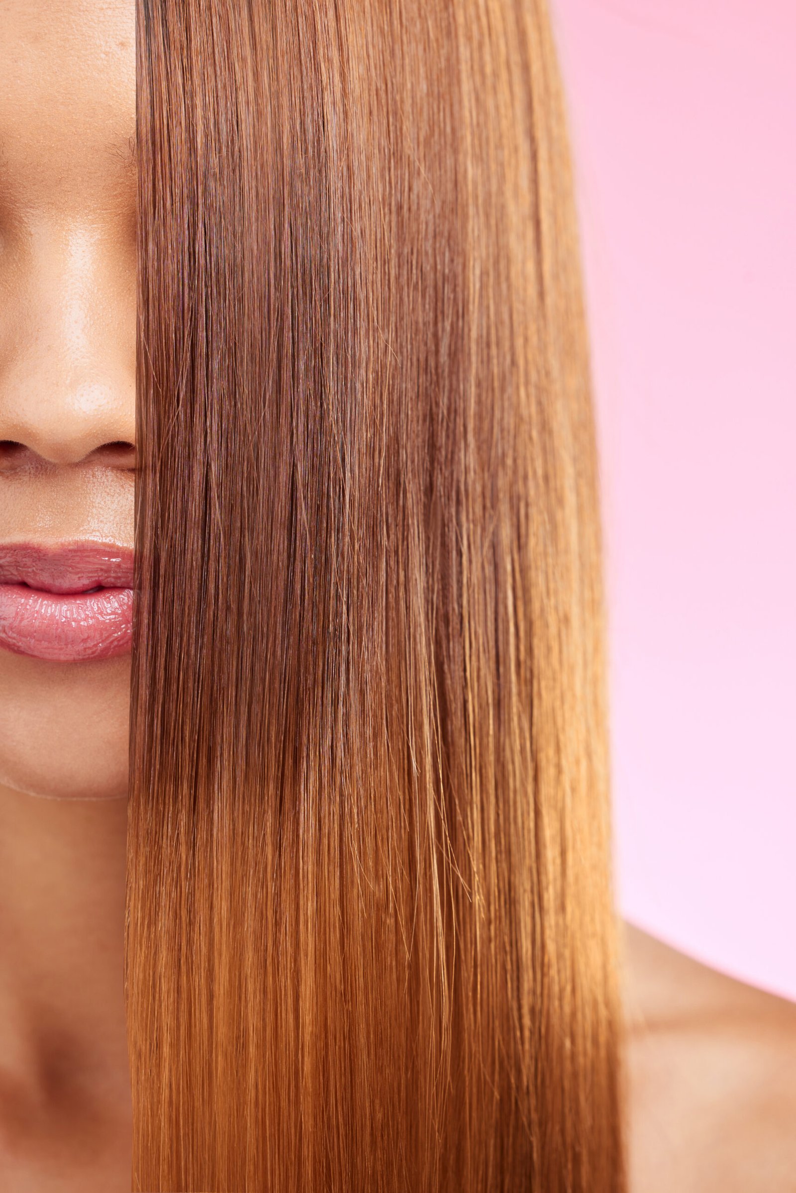 A woman with long, styled hair poses in front of a pink background, highlighting the benefits of a keratin treatment.