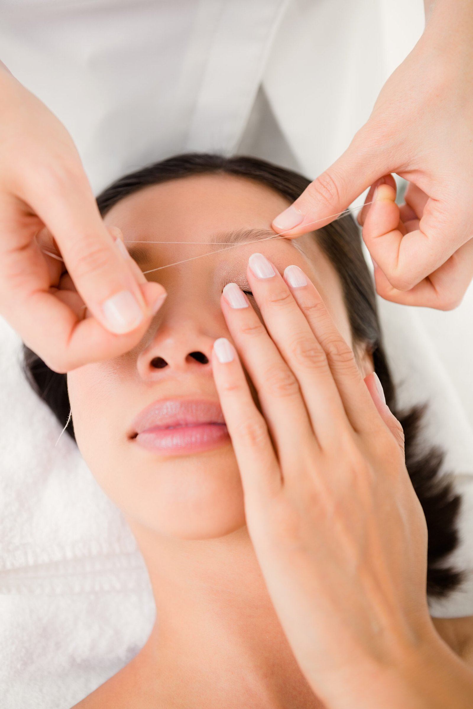 A woman receiving a facial treatment while threading her eyebrows, showcasing relaxation and self-care.