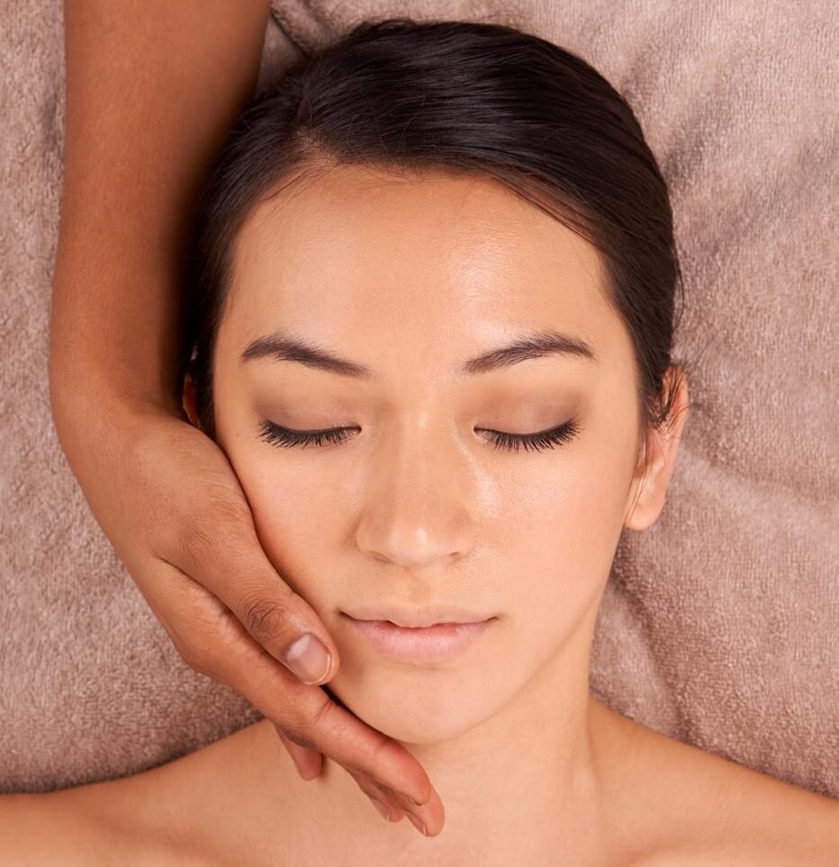 A woman enjoys a relaxing facial massage, her eyes closed and a serene expression on her face.