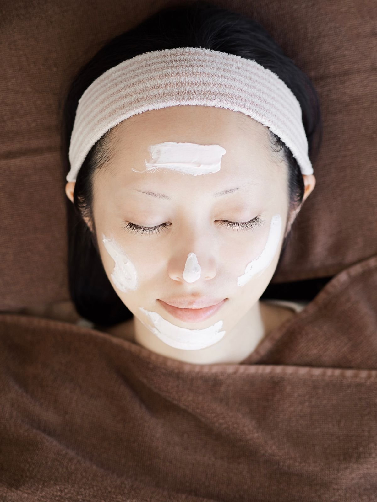 A woman elegantly wearing a face mask, showcasing a serene expression and a touch of luxury in her beauty routine.