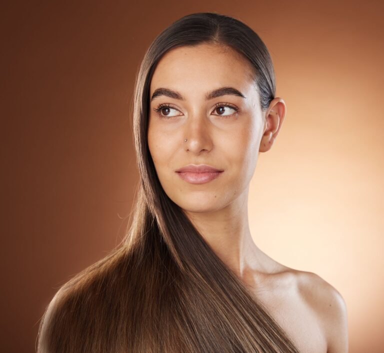 A woman with luxurious long hair poses against a warm brown background, highlighting her exquisite hair coloring.