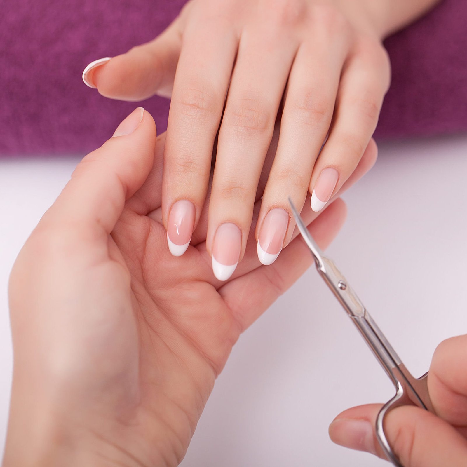 A woman is having her nails trimmed with scissors at a nail salon, showcasing a focus on personal grooming and care.