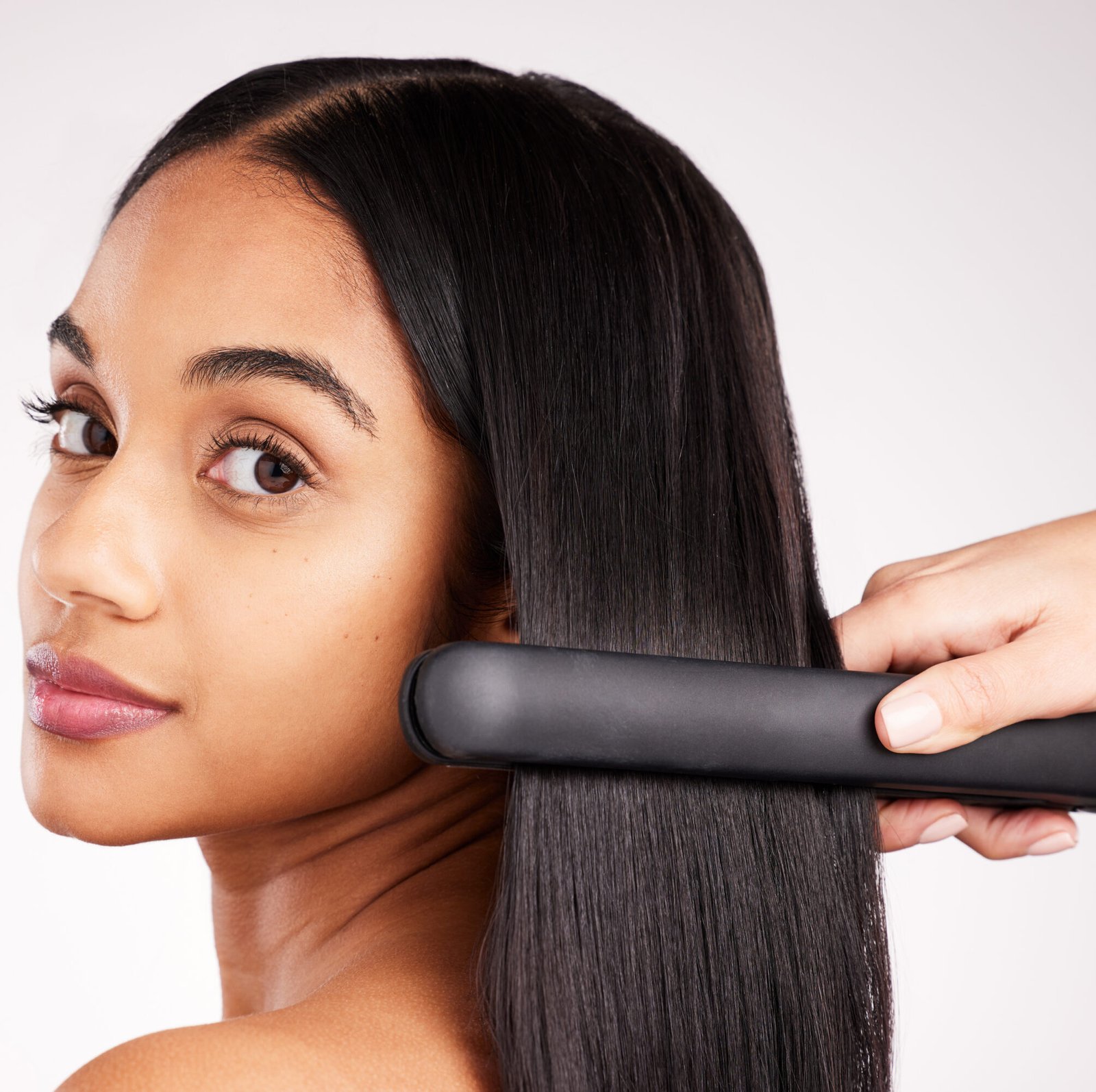 A woman is getting a hair straightener applied to her hair, aiming for a smooth and polished hairstyle.