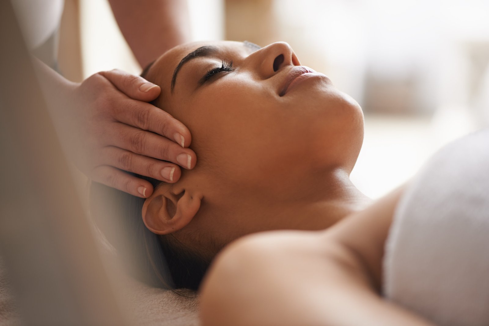 A woman enjoys a soothing facial and head massage at a tranquil spa setting.