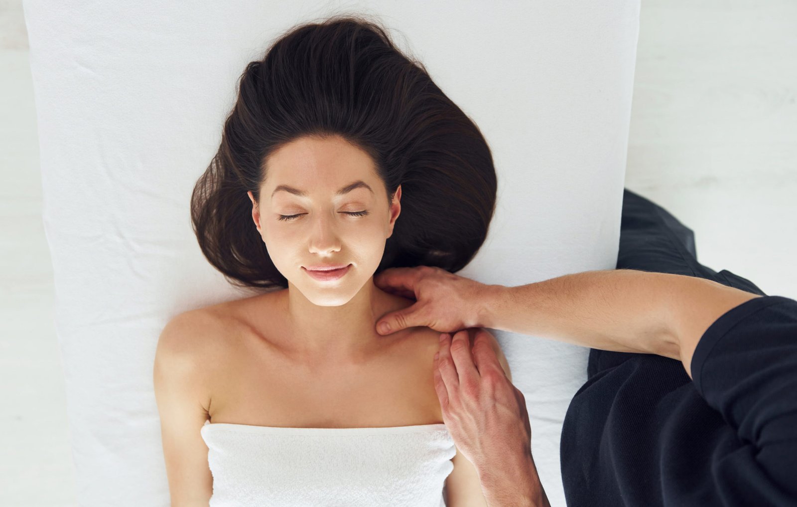 A woman relaxing during a shoulder massage at a spa, with soothing ambiance and professional therapist in the background.