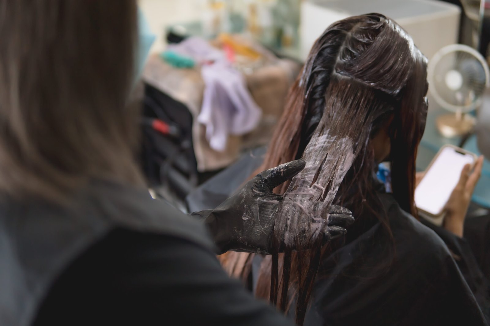 A woman receiving a hair coloring treatment at a salon, with a stylist applying products.