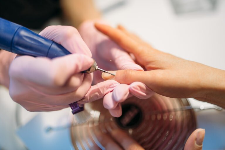 A person files a client's acrylic nails at a nail salon, focusing on achieving a smooth and polished finish.