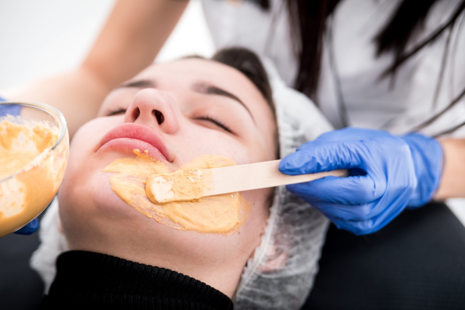 A woman receives a facial mask in a beauty salon, with facial waxing tools next to her.