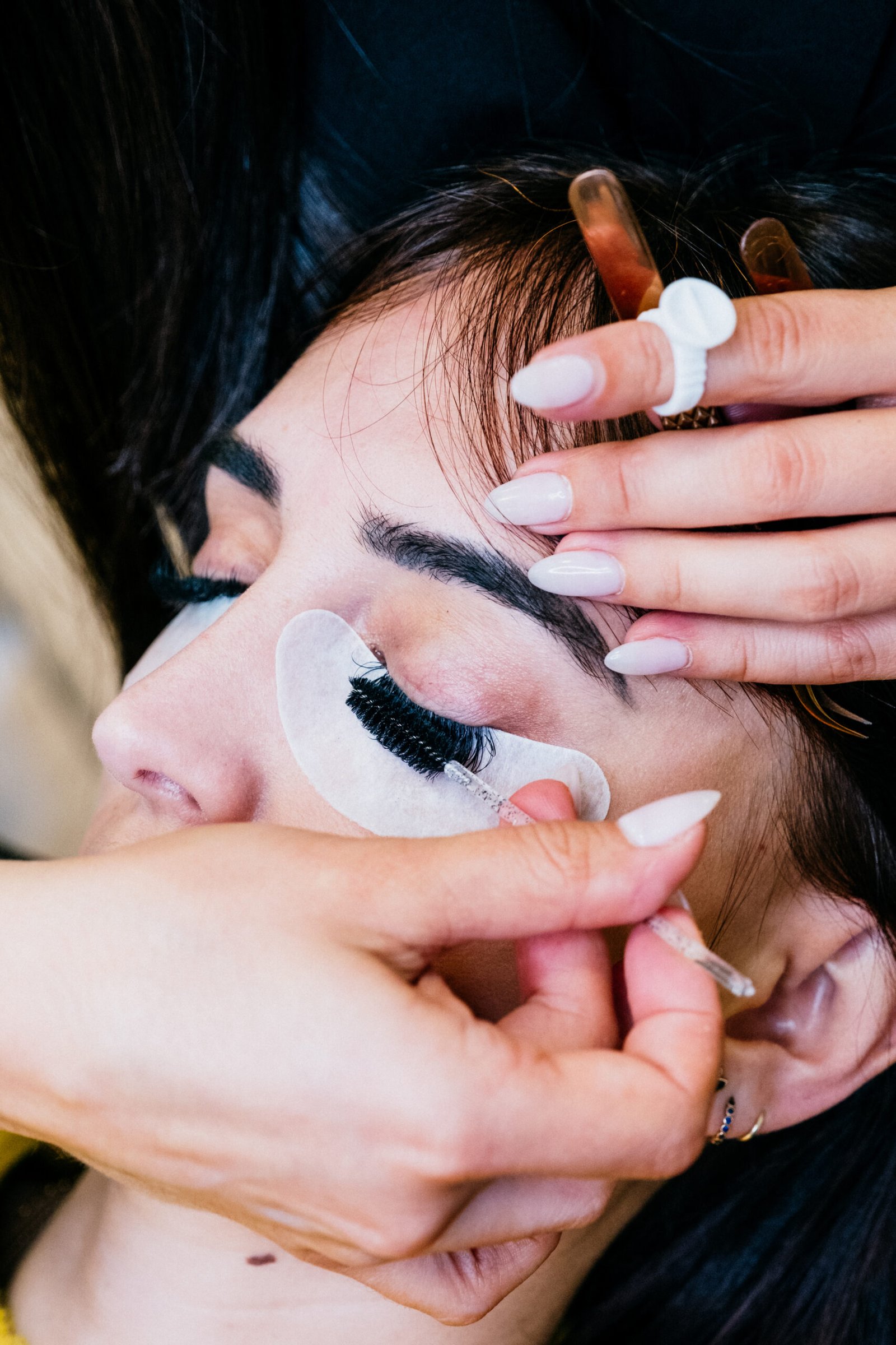 Close-up of a woman receiving eyelash extensions, with her eyes closed while a technician carefully applies individual lashes.