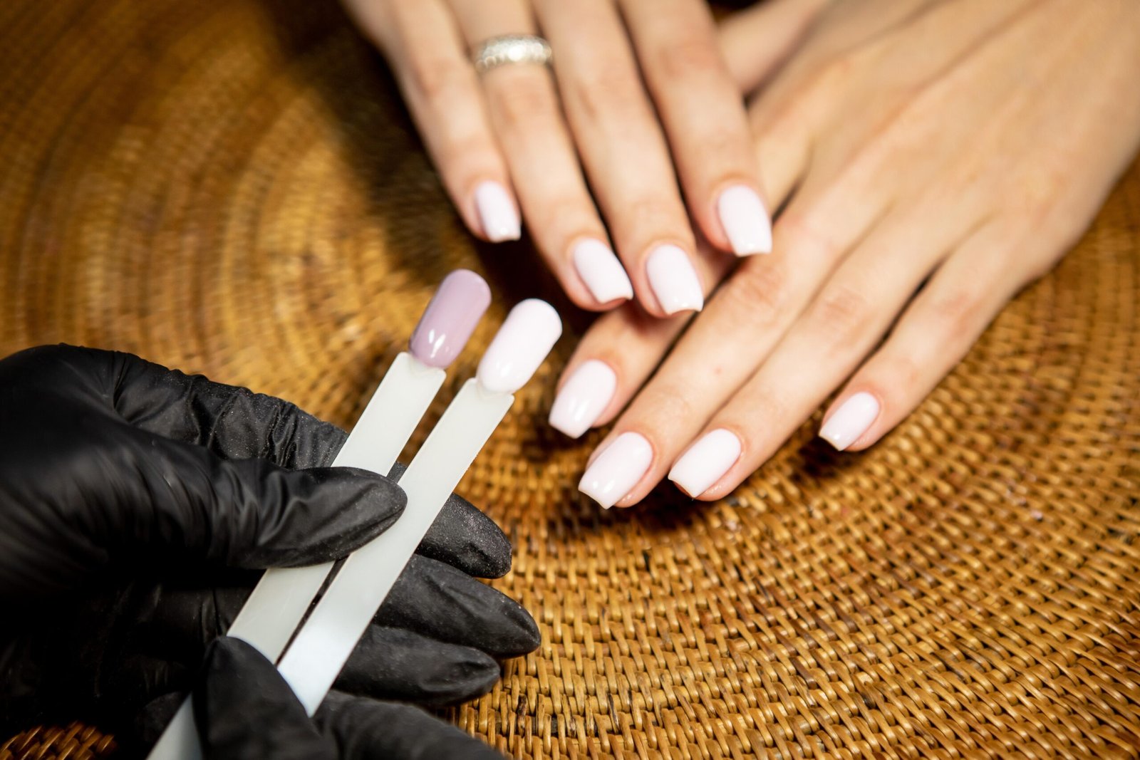 A woman with white manicured nails receives nail extensions at a salon, focusing on her hands during the process.