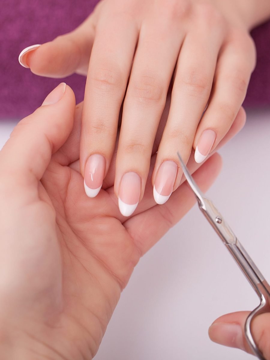 A woman is having her nails trimmed with scissors at a nail salon, showcasing a focus on personal grooming and care.