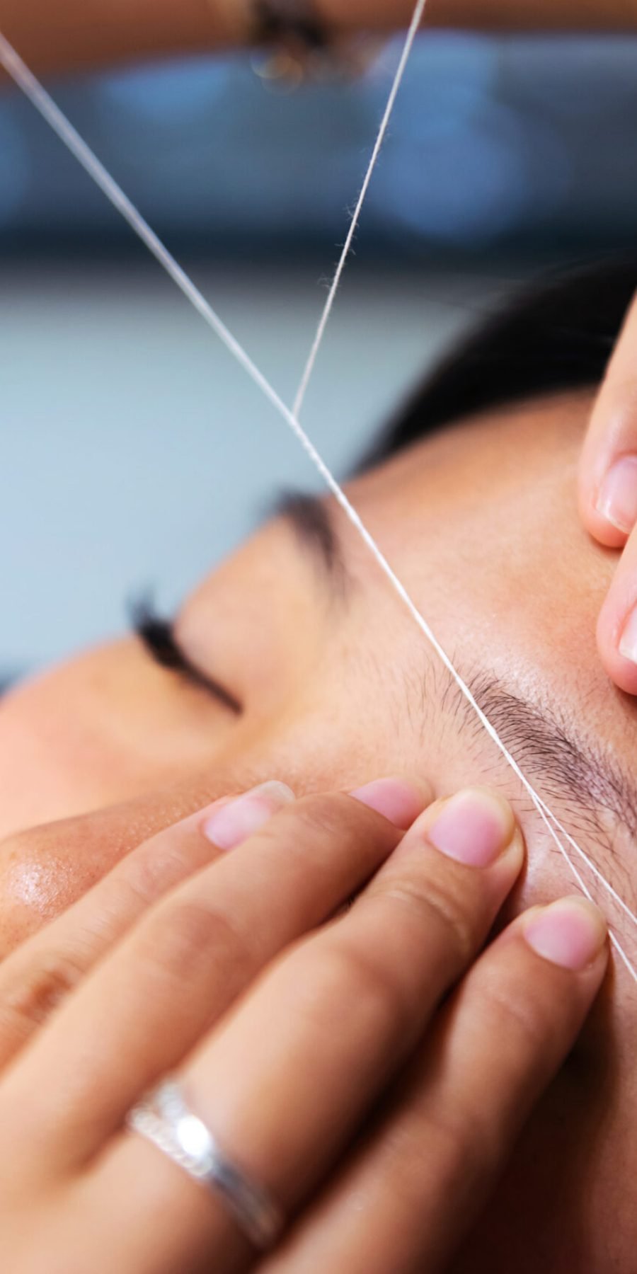 A salon expert carefully trims a woman's eyebrows using a thread, focusing on precision and technique in a well-lit setting.