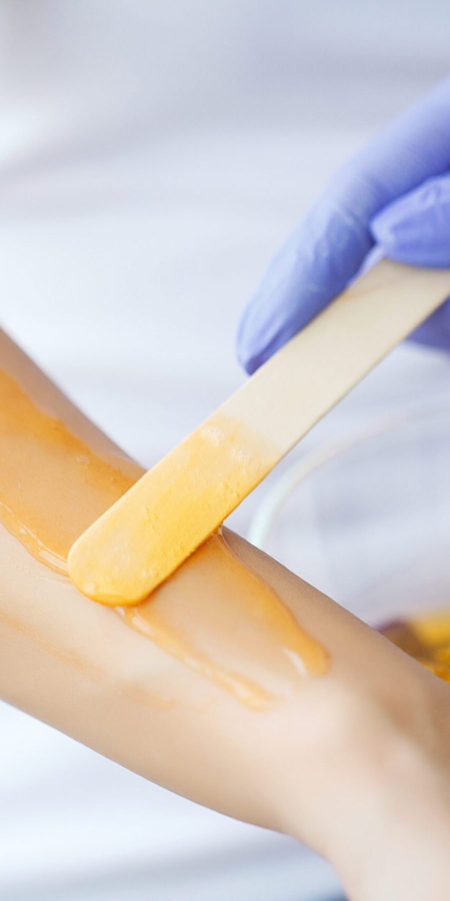 A woman at a salon gets honey wax applied to her forearm for hair removal.
