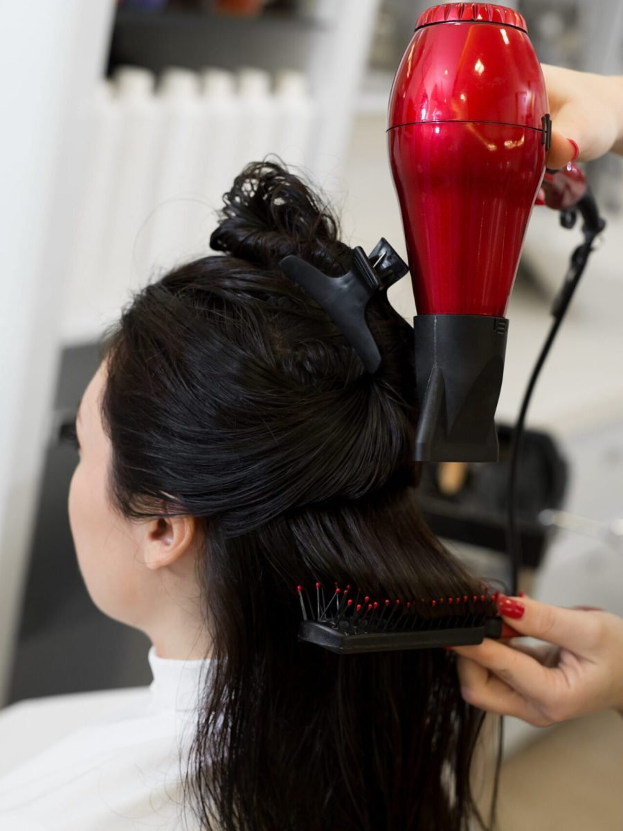 A woman blow dries her client's long hair, focusing on styling while holding the hairdryer with one hand.