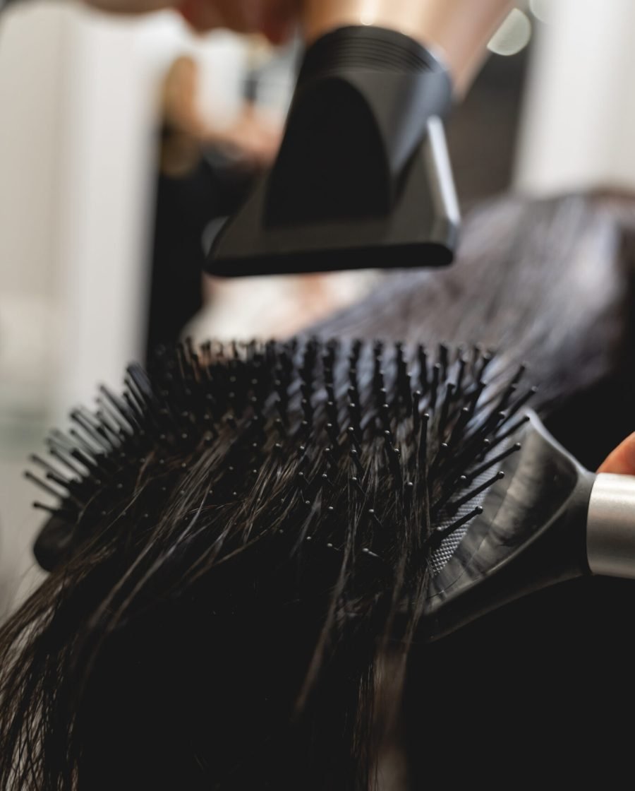 Individual at a salon blow drying their client's hair, skilfully using a hair dryer and comb for a stylish finish.