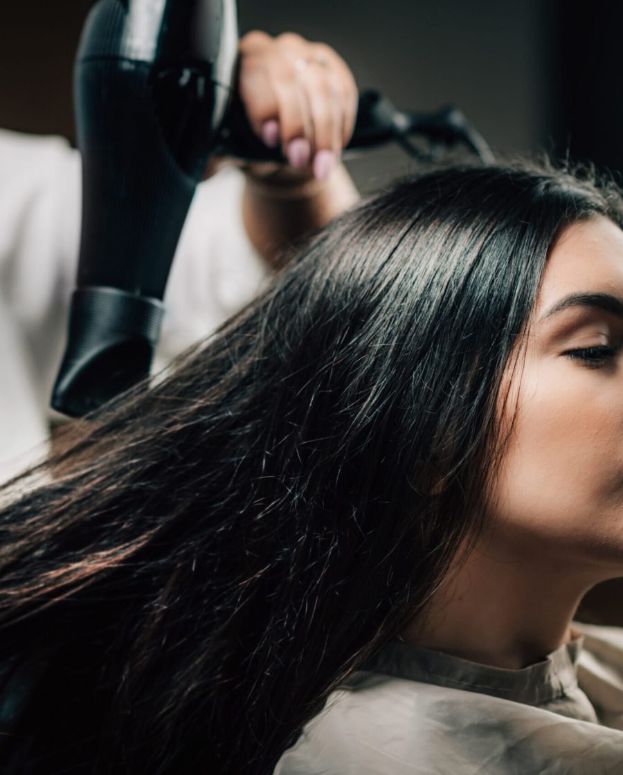 In a salon, a hairdresser blow-dries a woman's long hair, showcasing a professional styling session.