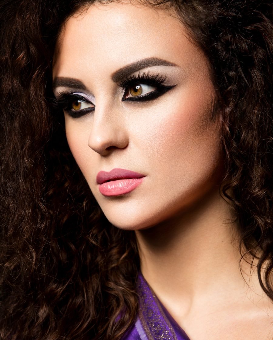 Stunning woman with curly hair, vibrant purple makeup, and bold graphic eyeliner, perfect for a party look.