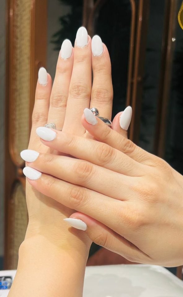 Close-up of a woman's hands featuring pristine white nails and stylish rings, reflecting meticulous nail care and elegance.