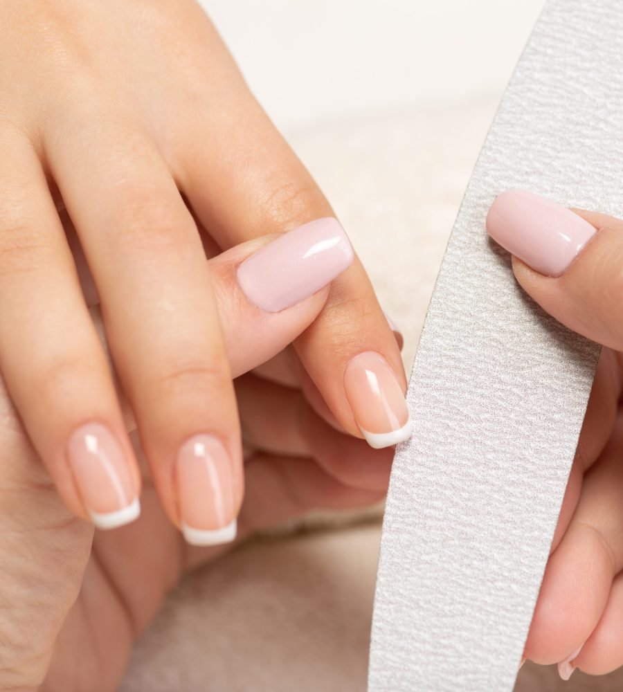 Close-up of a professional French manicure with natural pink base and white tips, nail technician filing nails in a salon setting.